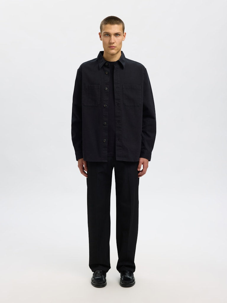 Male model wearing a black Twill overshirt by SELECTED Homme, featuring button-up front, two chest pockets, and a relaxed minimalist fit.