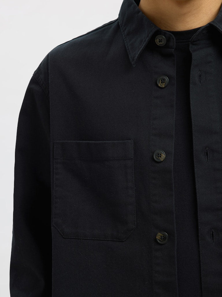 Male model wearing a black Twill overshirt by SELECTED Homme, featuring button-up front, two chest pockets, and a relaxed minimalist fit.