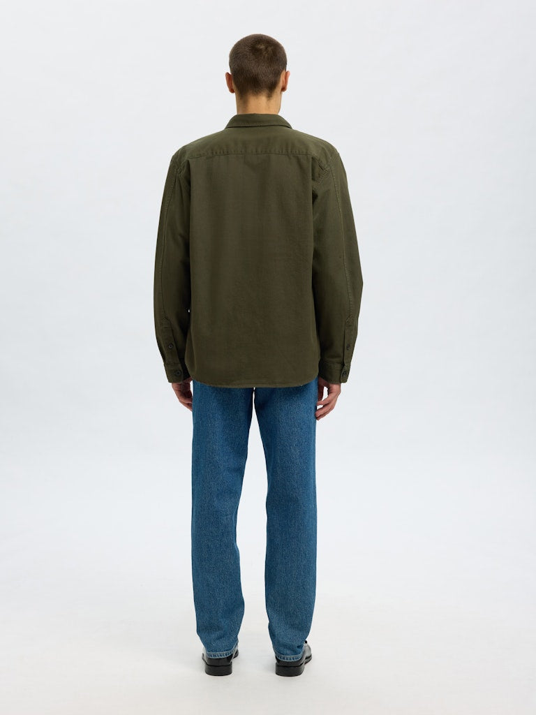Male model wearing a Forest Green twill overshirt by SELECTED Homme, featuring button-up front, two chest pockets, and a relaxed minimalist fit.