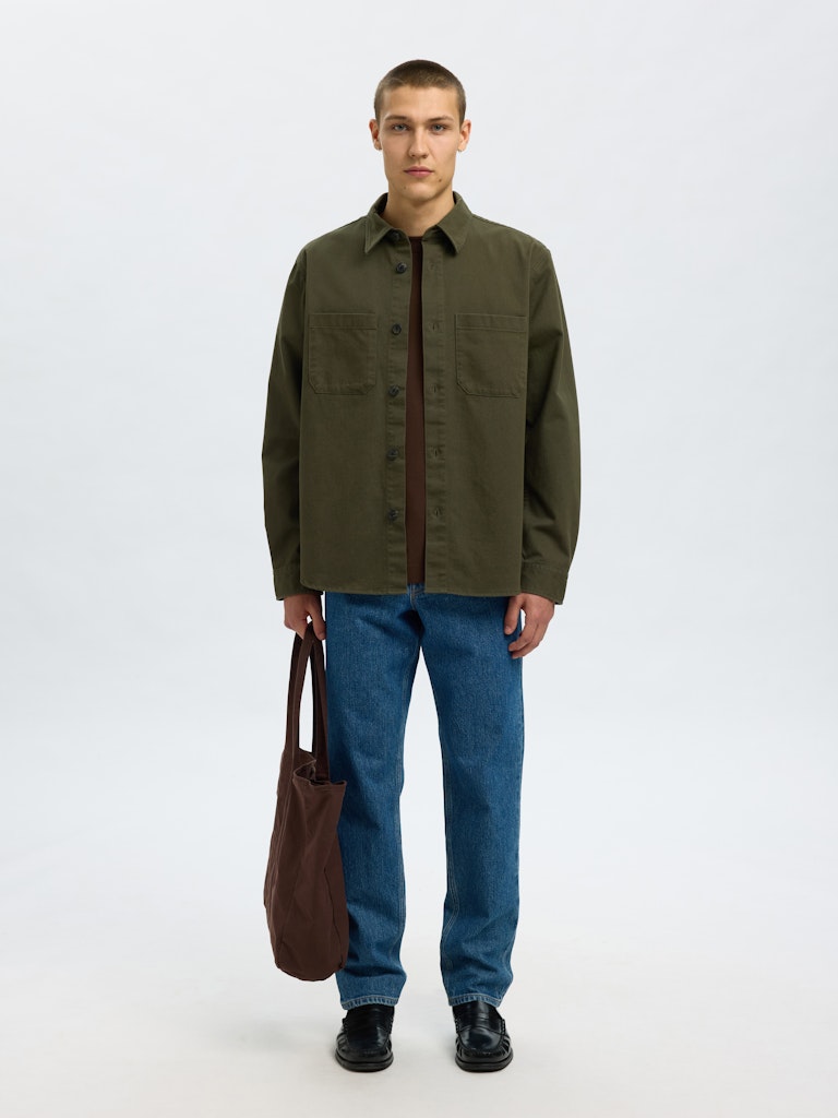 Male model wearing a Forest Green twill overshirt by SELECTED Homme, featuring button-up front, two chest pockets, and a relaxed minimalist fit.
