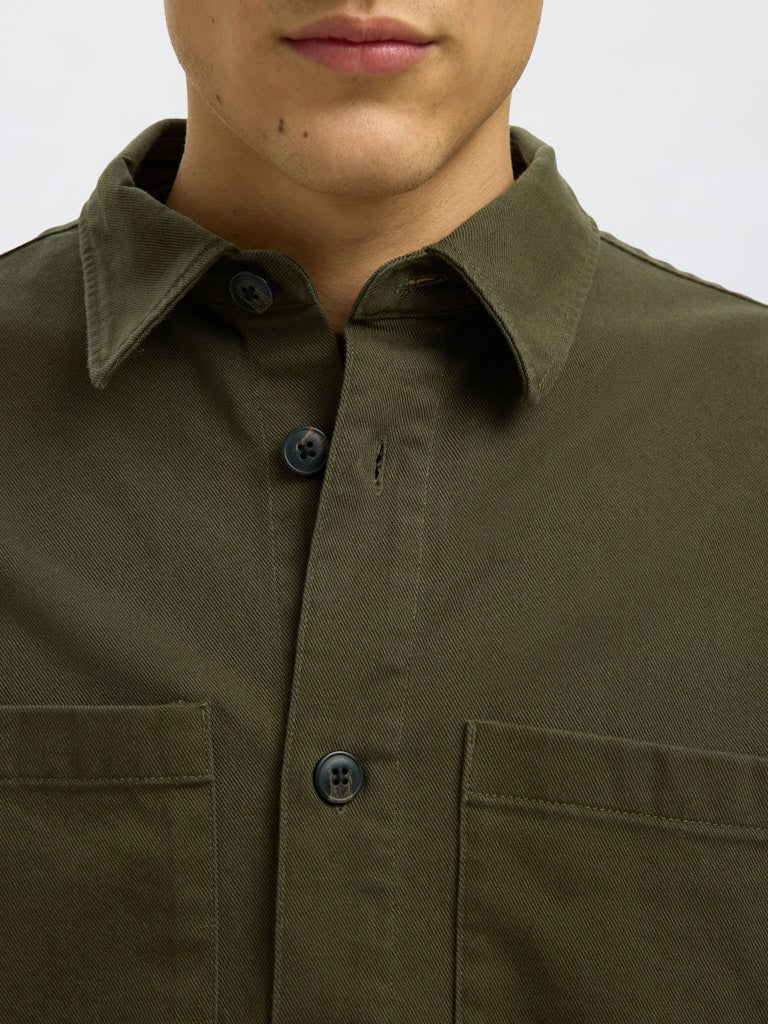 Male model wearing a Forest Green twill overshirt by SELECTED Homme, featuring button-up front, two chest pockets, and a relaxed minimalist fit.