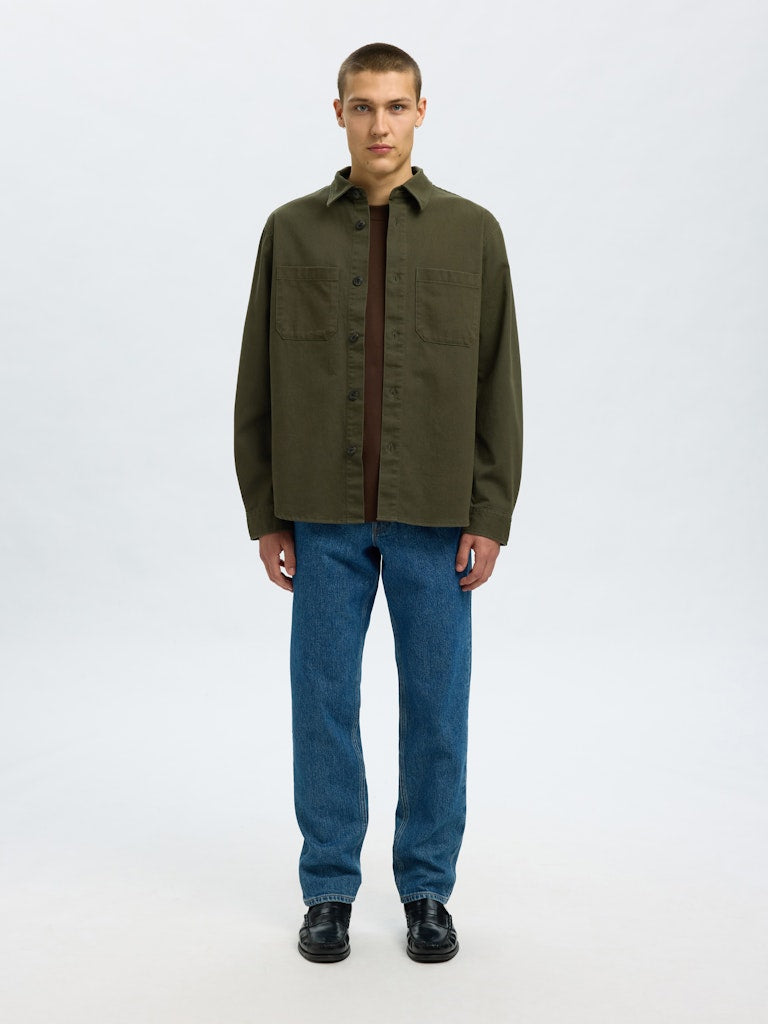 Male model wearing a Forest Green twill overshirt by SELECTED Homme, featuring button-up front, two chest pockets, and a relaxed minimalist fit.