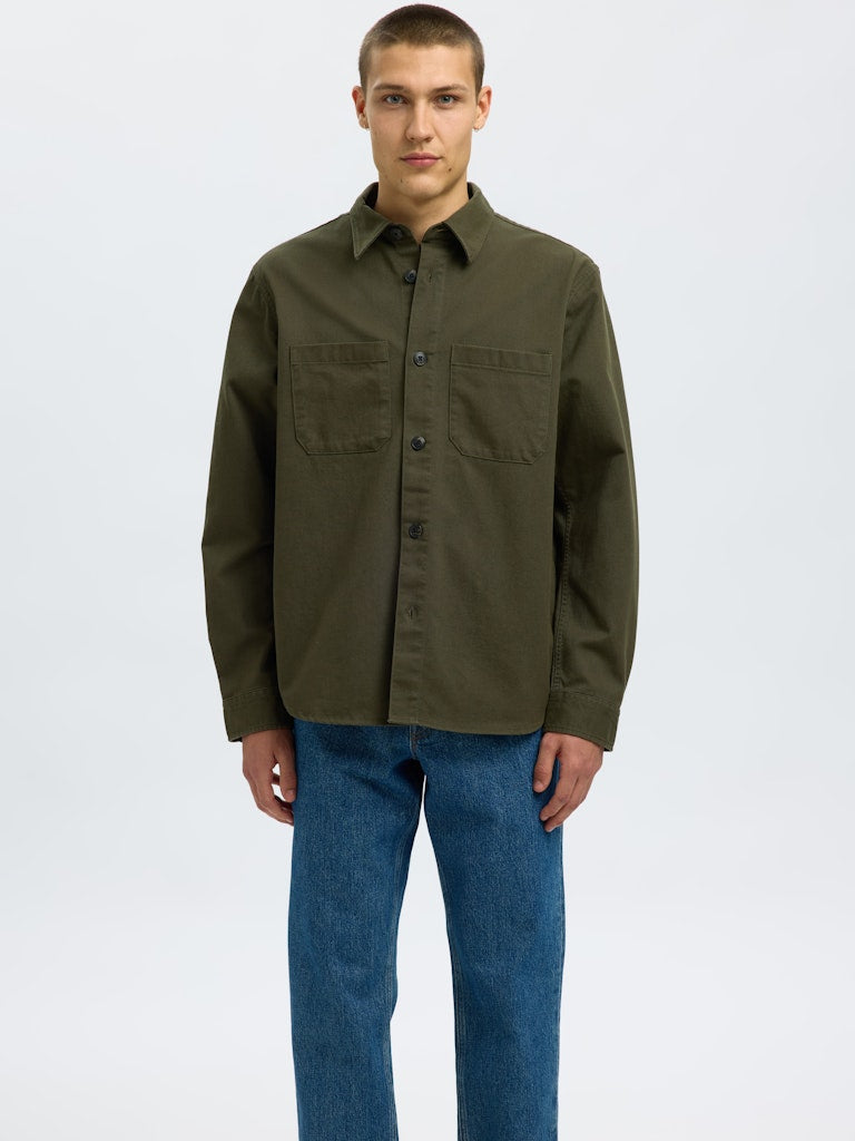 Male model wearing a Forest Green twill overshirt by SELECTED Homme, featuring button-up front, two chest pockets, and a relaxed minimalist fit.