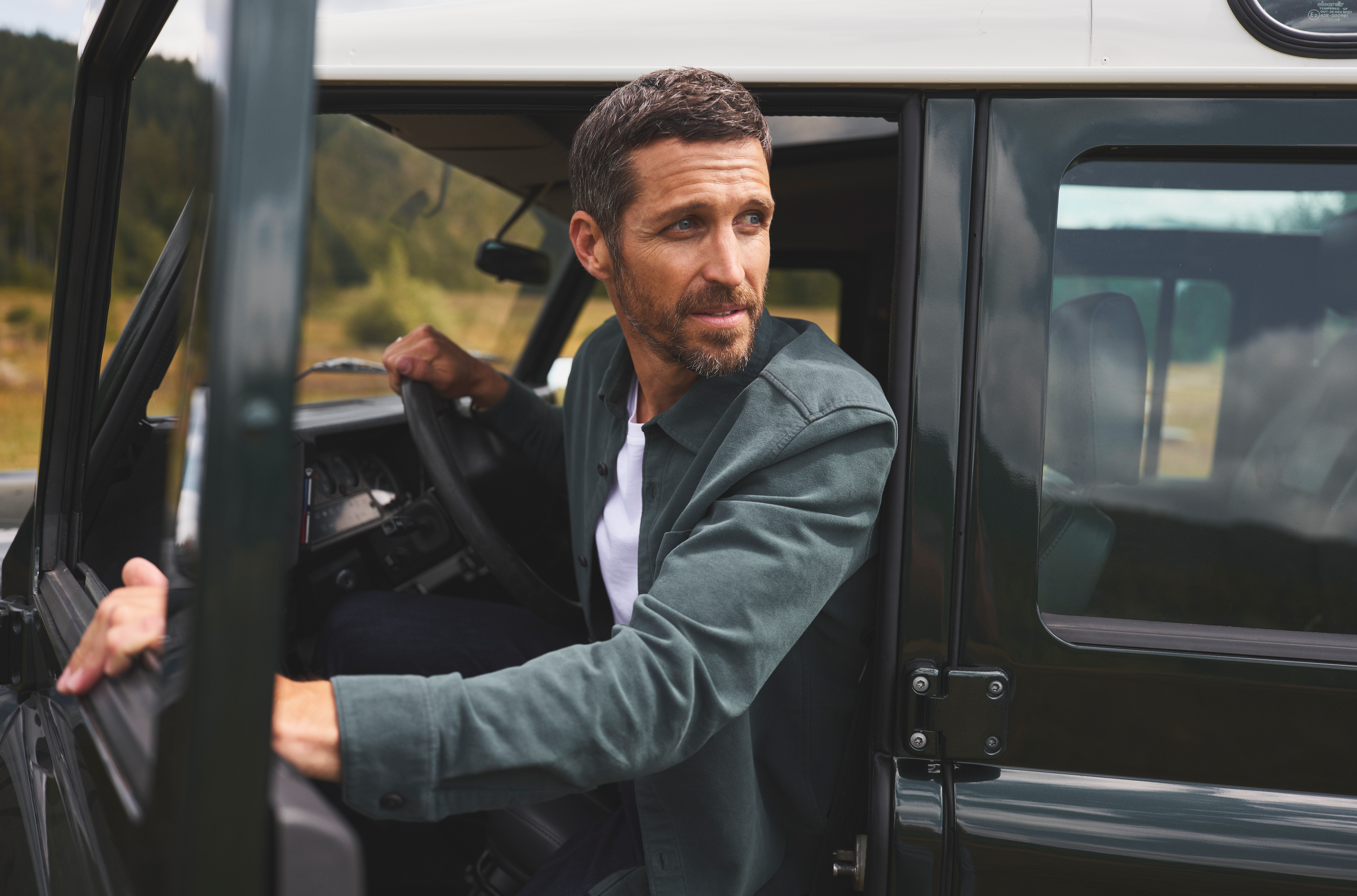 Man wearing a green overshirt by Duer Jeans sitting in a vehicle with a natural landscape in the background